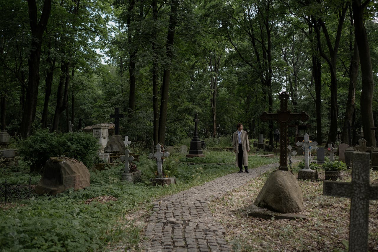 A solitary person walks through a lush, verdant cemetery, creating a serene and contemplative scene.