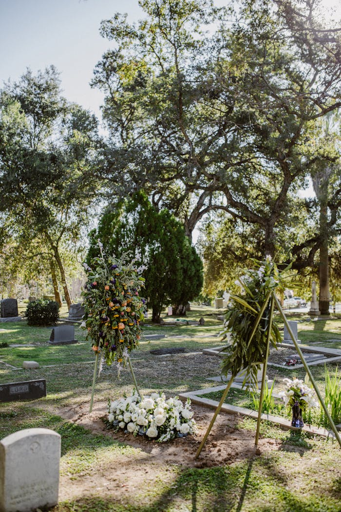 A tranquil cemetery with floral arrangements under a canopy of trees during daytime.
