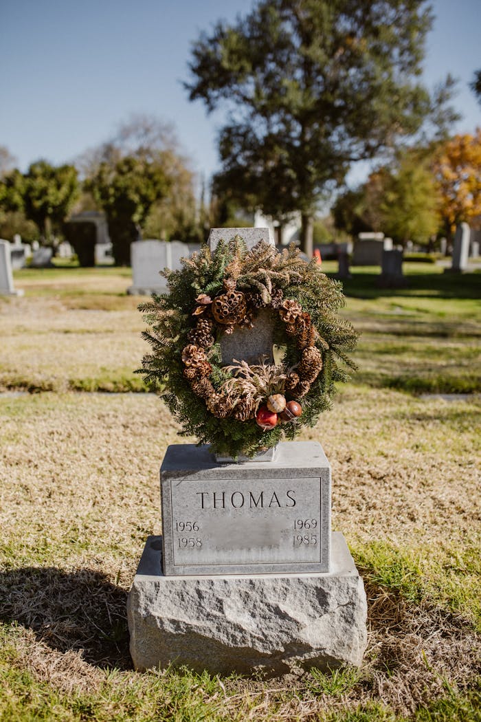 Tombstone with a decorative wreath in a peaceful cemetery setting under bright sunlight.