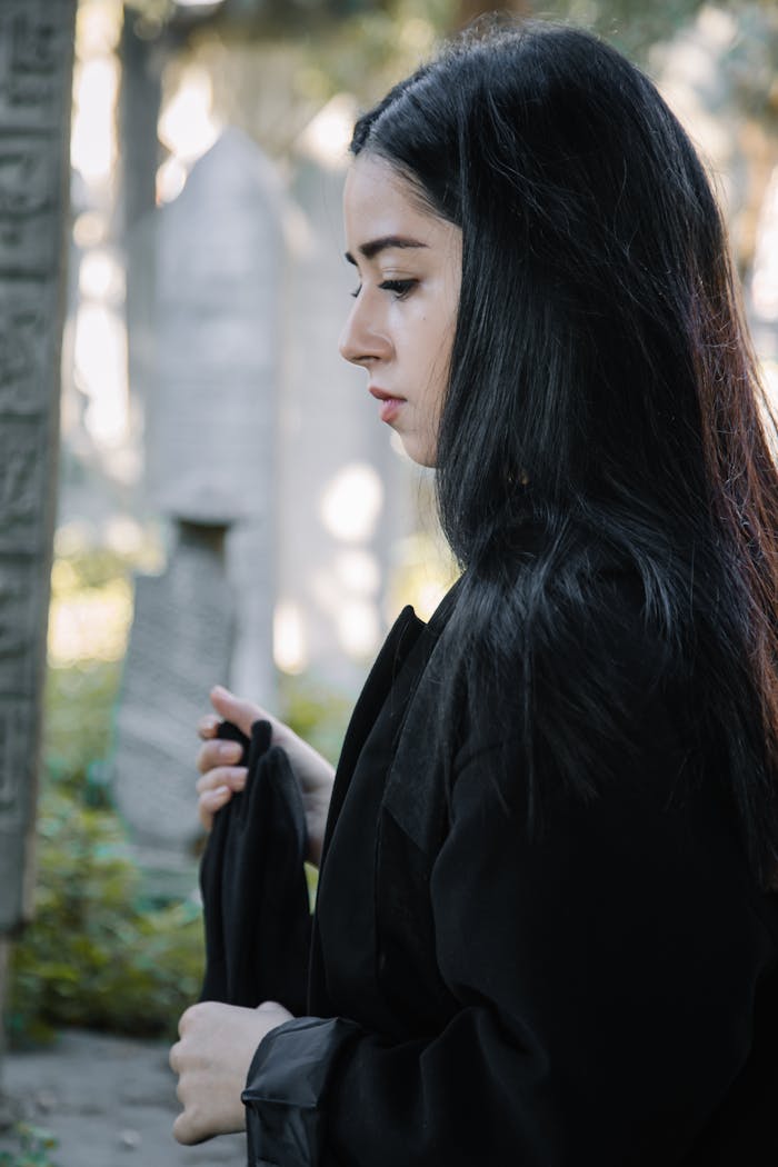 A contemplative young woman stands in a serene cemetery setting, reflecting on memories.